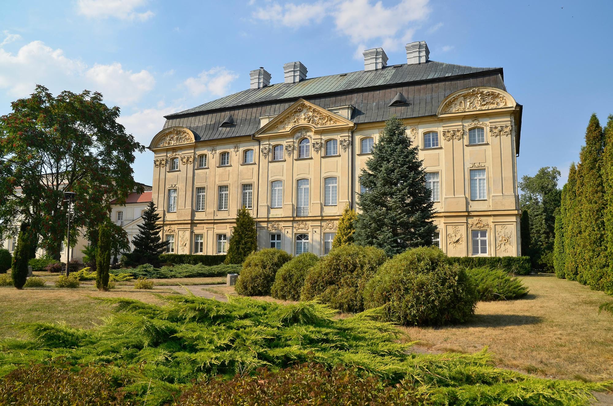 Piękny pałac z decorative detalami, otoczony zielonymi drzewami i krzewami pod błękitnym niebem