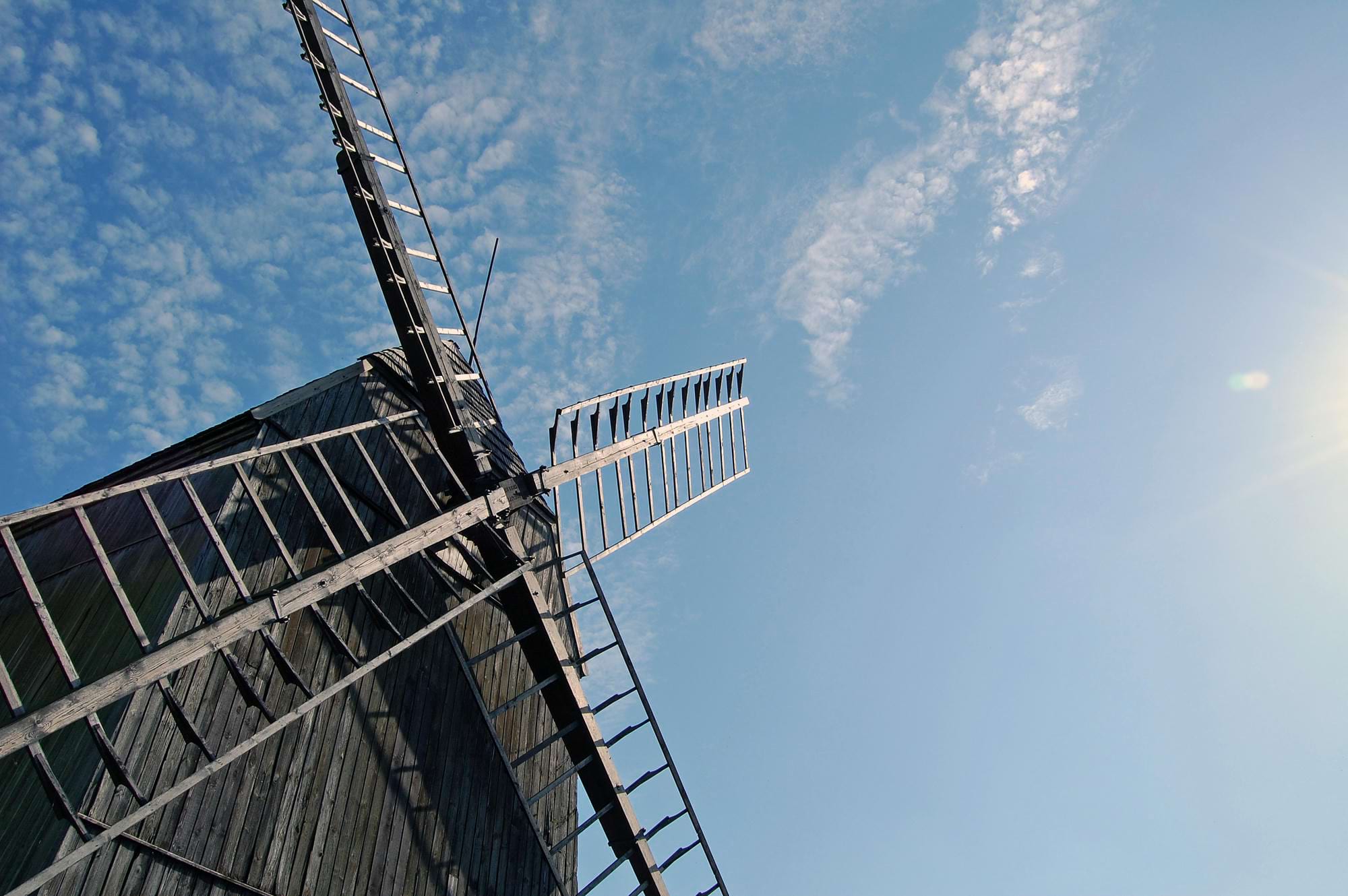 Stary wiatrak z drewna na tle niebieskiego nieba z chmurami i słońcem