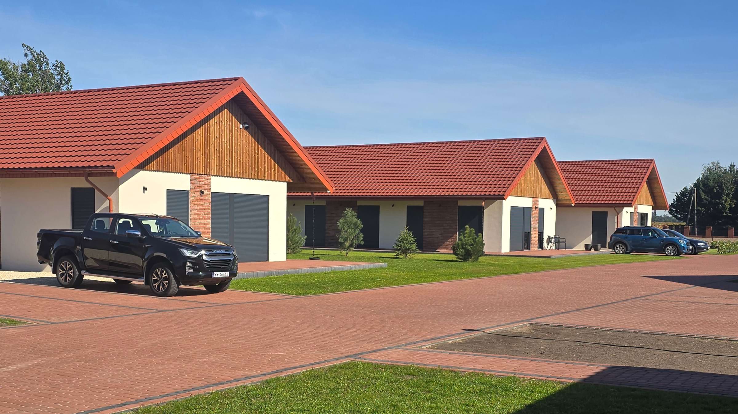 Nowoczesny budynek z czerwonymi dachami, parking i zielony trawnik pod jasnym, błękitnym niebem